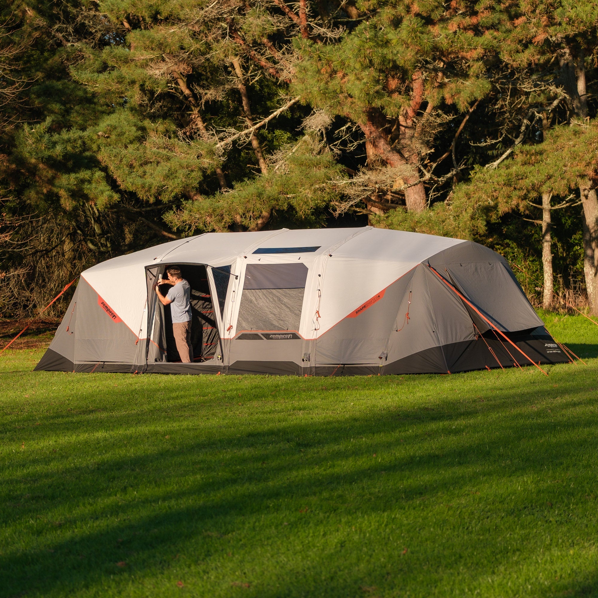 Large gray tent with orange accents set up on a grassy area with trees in the background