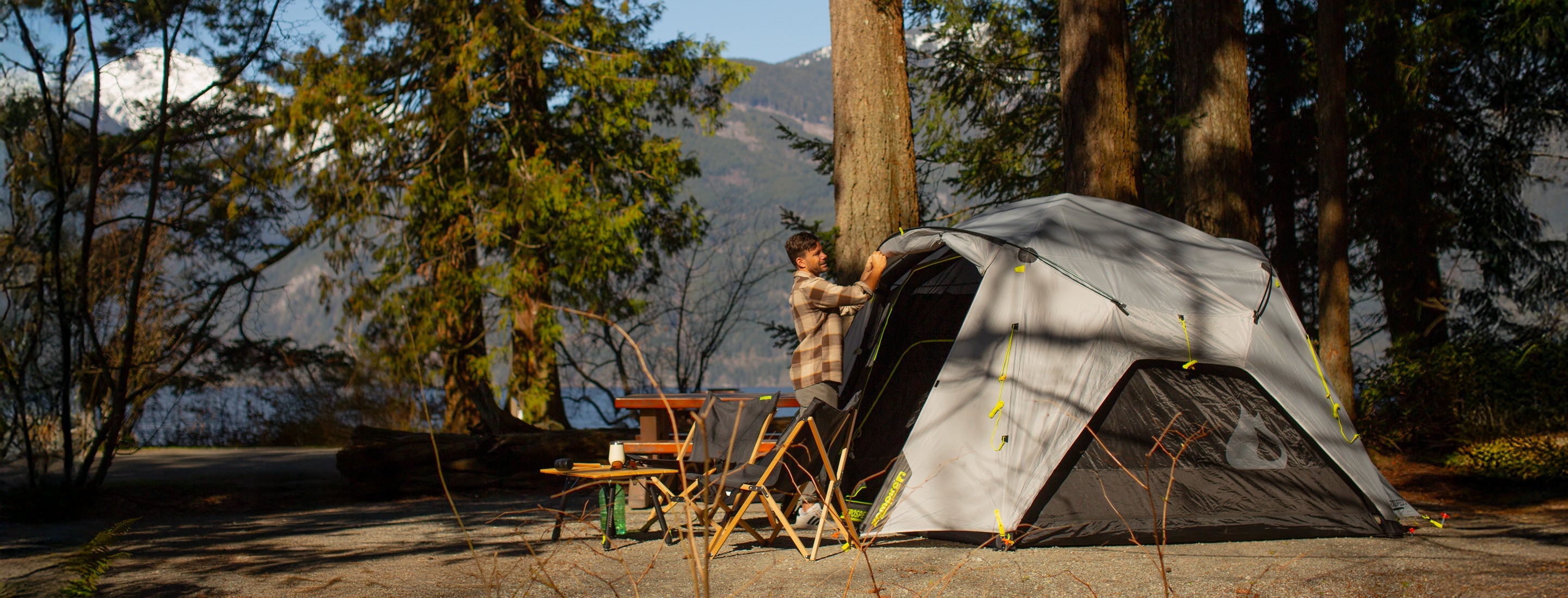 Person setting up a tent in a forested area with mountains in the background