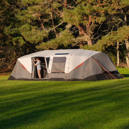 Large gray tent with orange accents set up on a grassy area with trees in the background