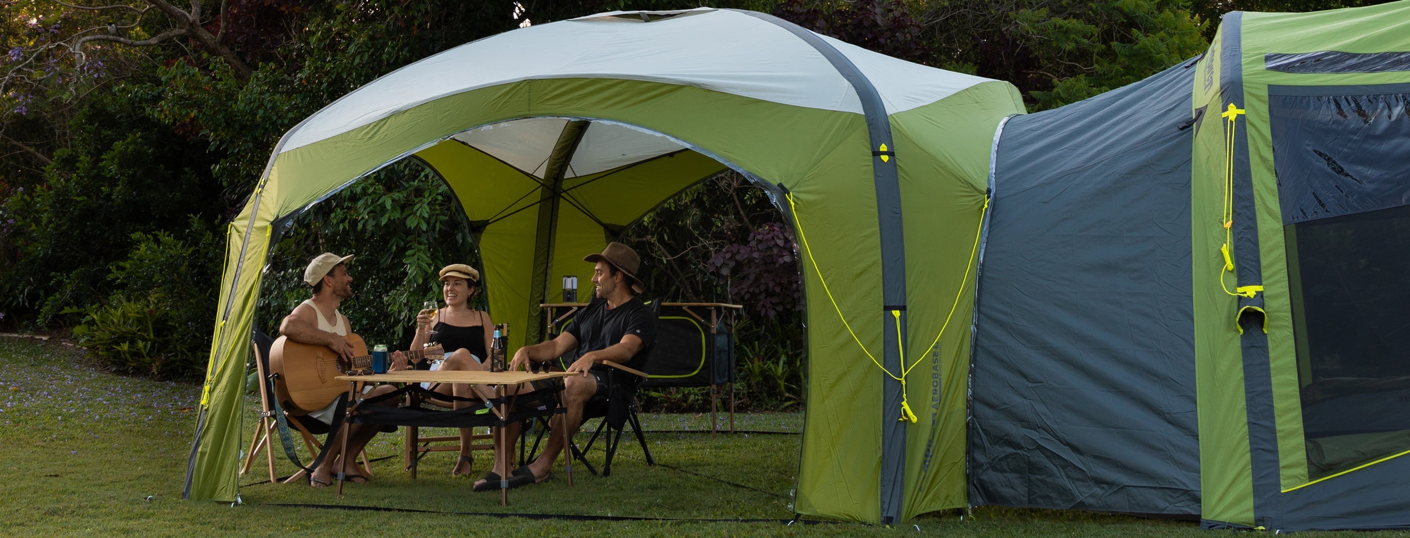People sitting at a table under a green air gazebo in a forest setting.
